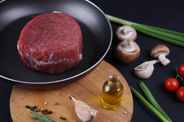 Rauw rundvlees vlees stesk in nonstick koekenpan, groenten, kruiden en olijfolie. Achtergrond, Heide eten concept koken. — Stockfoto