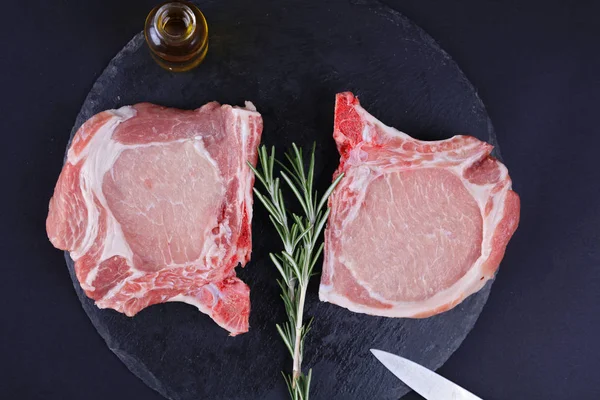 Raw pork loin chops black background, spices. Cooking background, healthy eating concept.