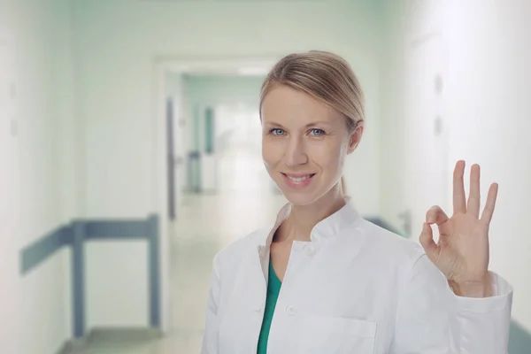 Усміхнена жінка-лікар, що показує "Добре" або "Вправо" на лікарняному фоні. Охорона здоров'я та медична концепція — стокове фото