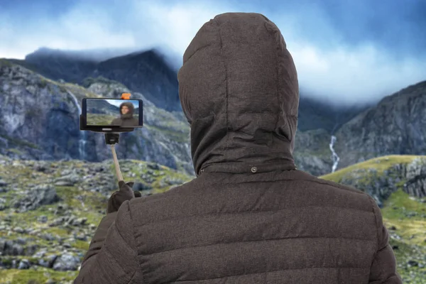 Hombre tomando una selfie en el paisaje de montaña con móvil, teléfono celular y selfie stick — Foto de Stock