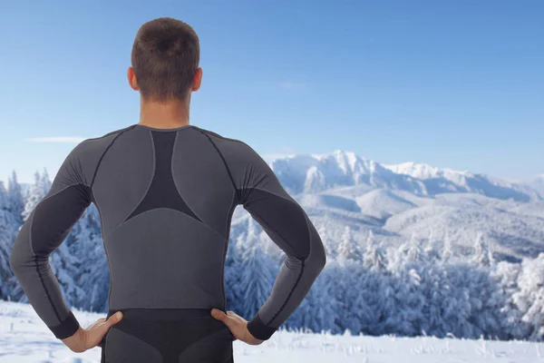 Fitness muscular man standing before or after winter workout exercising in snowy mountain. Preparing for or rest after sport activity. Sport, recreation and healthy lifestyle concept