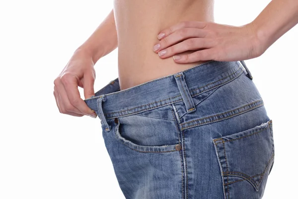 Ernährungsmotivation und erfolgreiches Konzept zur Gewichtsreduktion. Nahaufnahme der schlanken Taille einer jungen Frau, die große Jeans auf weißem Hintergrund trägt — Stockfoto