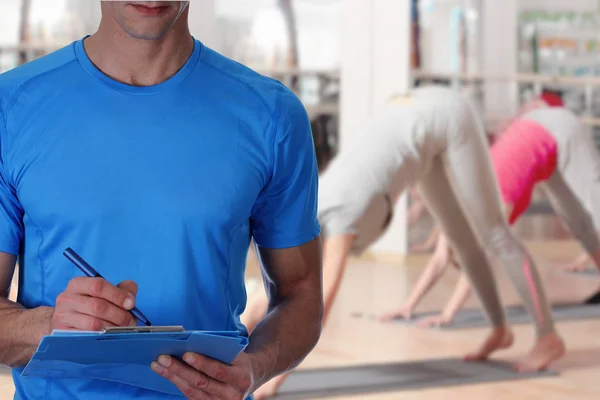 Fitness trainer with workout plan close up in gym background. Sport, fitness and healthy life style concept.