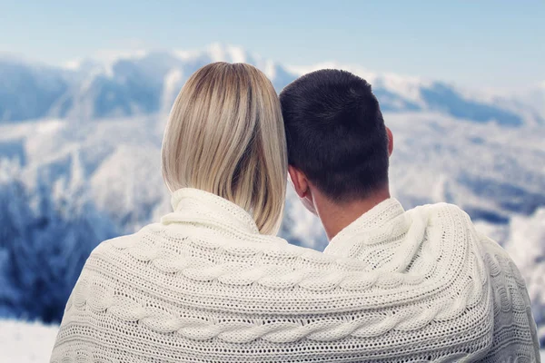 Couple in love covered with blanket enjoying mountain view on winter holiday vacation