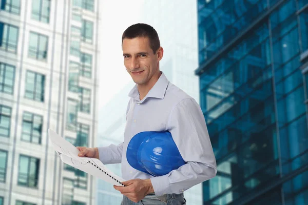 微笑的建筑师举行蓝图和头盔办公大楼前的肖像 — 图库照片
