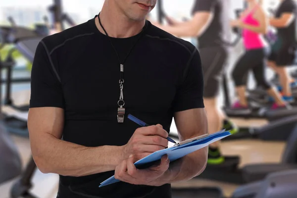 Fitness trainer with workout plan close up in gym. Sport, fitness and healthy life style concept.