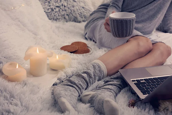 Gemütlicher Abend, warme Wollsocken, weiche Decke, Kerzen. Frau entspannt sich zu Hause, trinkt Kakao, benutzt Laptop. Bequemer Lebensstil. — Stockfoto