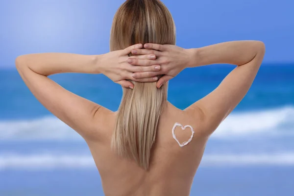 Mujer disfrutando del verano en vacaciones de verano en la playa cerca del mar con loción protectora del sol con forma de corazón en el hombro. Protección contra quemaduras solares — Foto de Stock