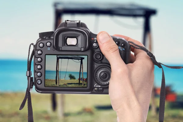 Male hand taking photo of a wooden swing on the beach with digital DSLR camera. — Stock Photo, Image