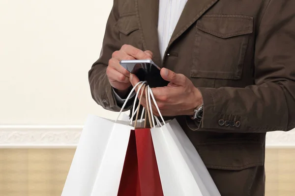 Hombre de compras. Hombre sosteniendo bolsas de la compra y usando el teléfono celular. Concepto de compras online . —  Fotos de Stock