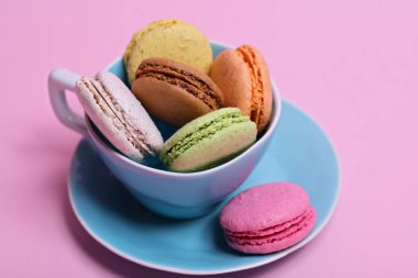 Bir fincan pembe bir arka plan üzerinde renkli farklı aromalı bademli kurabiye