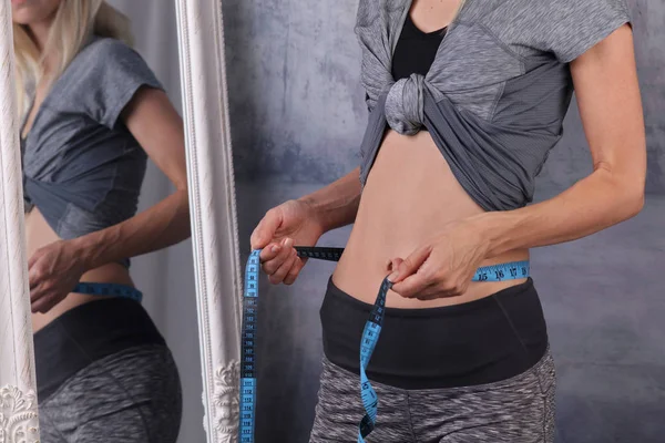 Форма, фитнес-женщина перед зеркалом проверки результатов тренировки и измерения ее талии с помощью ленты. Женщина с идеальными мышцами брюшной полости и извилистыми. Здоровое питание, диета и потеря веса — стоковое фото