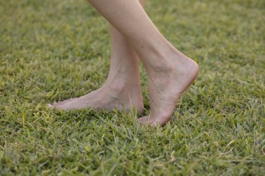 Genç kız gevşeme bahar güneşli park açık havada taze yeşil çim yürüyüş zevk yalınayak. Barefootism