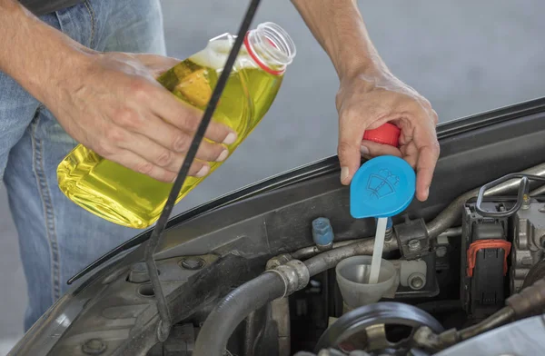 Scheibenflüssigkeit. Mann schüttet Flüssigkeit zur Scheibenreinigung in sein Auto. — Stockfoto