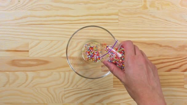 Woman pours multi-colored sugar sprinkles dots into a glass bowl, top view — Stock Video