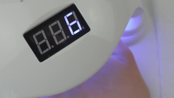 Jovem mulher secando esmalte dentro de uma lâmpada UV com vista superior do temporizador. Fechar as mãos — Vídeo de Stock