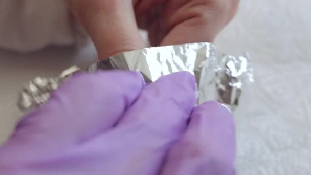 Una joven hace una manicura. Envuelve sus dedos en papel de aluminio para quitar el gel viejo. Manicura de uñas — Vídeos de Stock