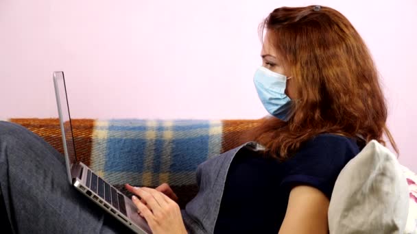 한 젊은 여성 이 격리중 의료용 마스크를 쓴 채 집에서 일하고 있습니다. 사회적 거리 — 비디오