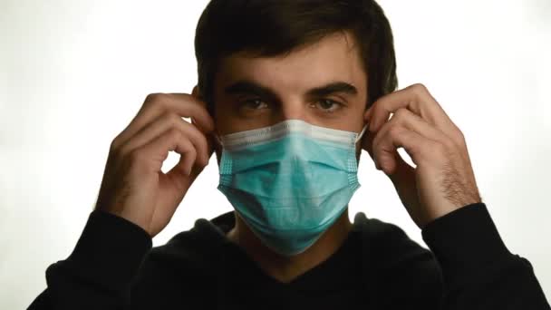 Retrato de um jovem tirando sua máscara médica e sorrindo em um fundo branco, isolar covid-19 — Vídeo de Stock