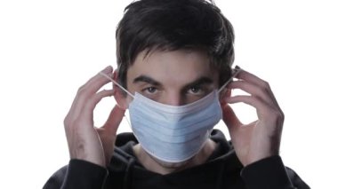 Beyaz arka planda tıbbi maske takan genç bir adamın portresi.