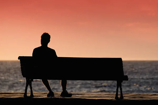 Силуэт молодых людей, сидящих в одиночестве на скамейке — стоковое фото