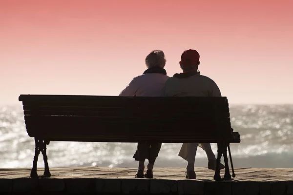 Silhouette anziani coppia in attesa di coloratissimo tramonto sulla panchina — Foto Stock