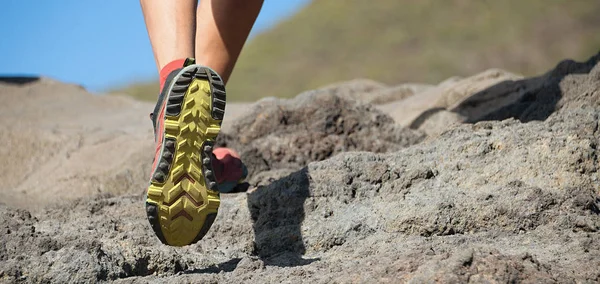 Athlete trail running in the mountains on rocky terrain, sports shoes detail