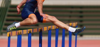 Stadyumda engelli koşu yapan bir atlet, atlet atletizm yarışında engelin üzerinden atlıyor.