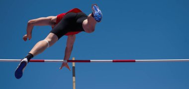 Mavi gökyüzü arka planında sırıkla atlayan erkek.