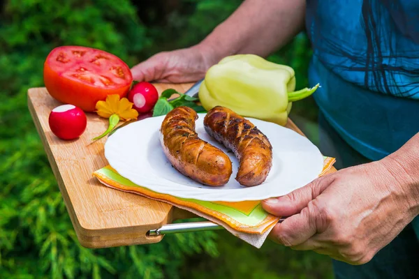 Female hands holding plate with grilled sausages in the garden
