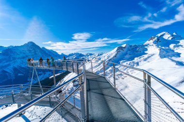 GRINDELWALD-FIRST, SWITZERLAND - JANUARY 15 2020: Tourists take photos on the Cliff Walk, a popular viewing platform on the First mountain in Grindelwald, which offers with stunning Alpine views