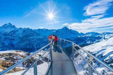 GRINDELWALD-FIRST, SWITZERLAND - JANUARY 15 2020: Tourists take photos on the Cliff Walk, a popular viewing platform on the First mountain in Grindelwald, which offers with stunning Alpine views