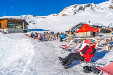 GRINDELWALD-FIRST, SWITZERLAND - JANUARY 15 2020: People at Schreckfeld on The First mountain admire stunning Alpine views and enjoy winter sports.