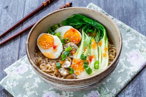 Japanese sesame ramen noodles with pok choi, boiled egg, mushrooms, spring onions and chili sauce