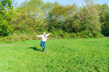 Orta yaşlı, koruyucu maskeli bir erkek parkta tek başına egzersiz yapıyor.
