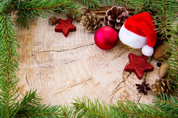 Weihnachtsmütze mit Christbaumkugel und Tannenzweigen auf Holzgrund. — Stockfoto