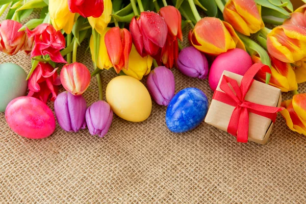 Весняні тюльпани з різнокольоровими великодніми яйцями та подарунковою коробкою . — стокове фото