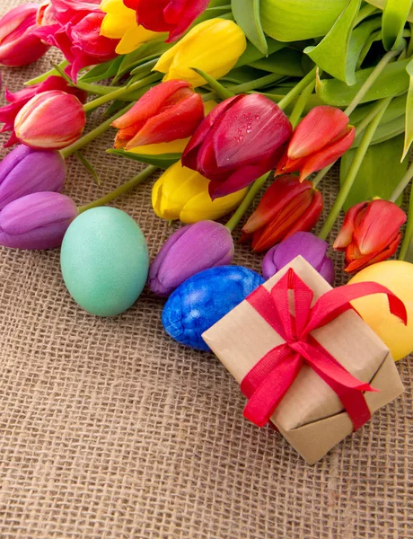 Весняні тюльпани з різнокольоровими великодніми яйцями та подарунковою коробкою . — стокове фото