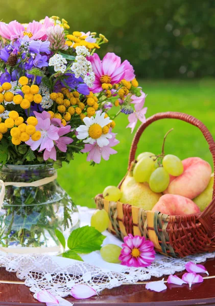 Bouquet colorful wild flowers and fruit basket. — Stock Photo, Image