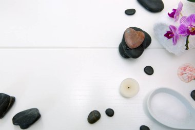Pembe orkideli spa seti, siyah taşlar ve beyaz ahşap arka planda mum..
