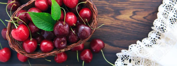 Kirschen im Korbtopf und Gänseblümchen auf altem Holzgrund. — Stockfoto