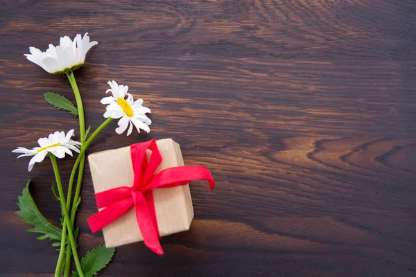 Marguerites blanches et boîte cadeau sur fond de bois brun . — Photo