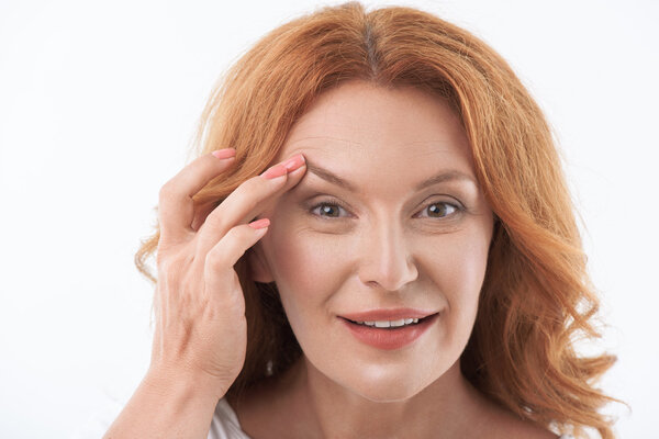 Веселая женщина средних лет довольствуется уходом за кожей
