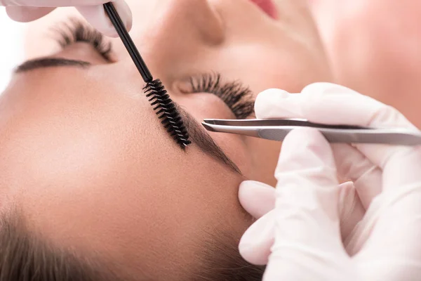 Skillful cosmetician pulling out brows