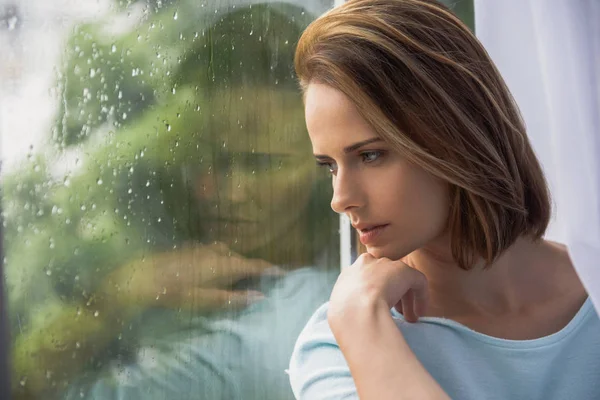 Разочарованная симпатичная девушка, сидящая перед окном — стоковое фото
