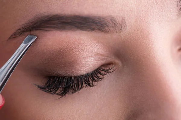 Young woman tweezing her eyebrows in beauty saloon — Stock Photo, Image