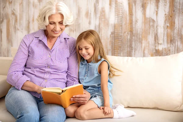 Venlig bedstemor og pige underholdende med bog derhjemme - Stock-foto