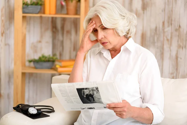 Frustrated mature lady reads paper — Stock Photo, Image