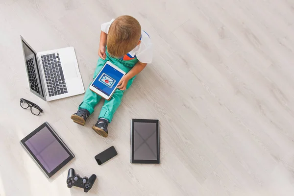 Menino sentado com aparelhos digitais em estúdio — Fotografia de Stock