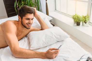 Neşeli adam akıllı telefon yatak odasında kullanarak